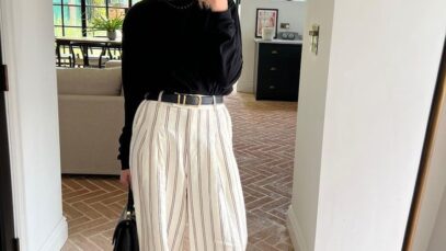 Mulher em um ambiente moderno, usando blusa preta e calças listradas brancas.